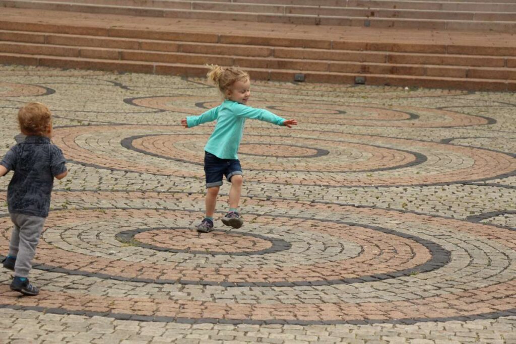 a 4-year old girl twirls in a plaza of circular tiles on a family trip to Norway in summer.