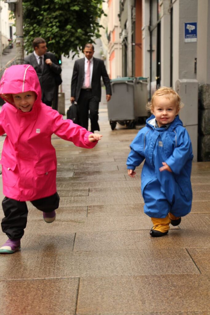 Two young children on a family trip to Norway wear full body rain suits to stay dry on rainy summer days.