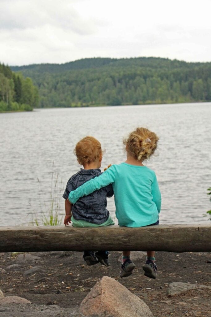 The Brewer kids, from the Family Can Travel blog, sit on a log and look at Sognsvann Lake while on a family trip to Oslo.