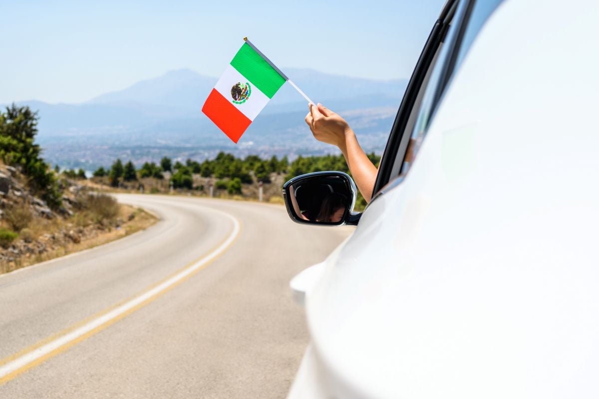 a driver holds a Mexican flag out the windo while driving in Mexico.