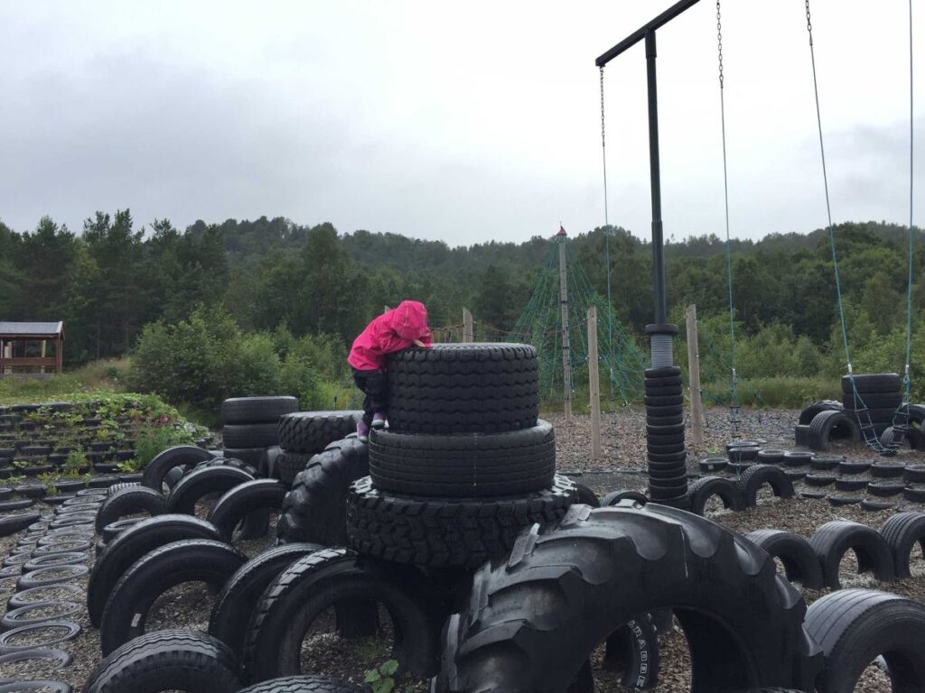 a 4-year old girl plays on the giant tires at an Aureosen Playground while on a family road trip in Norway.