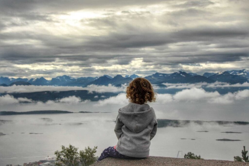 a 4-year old girl on a family road trip in Norway soaks in the mountain views at the Varden viewpoint.