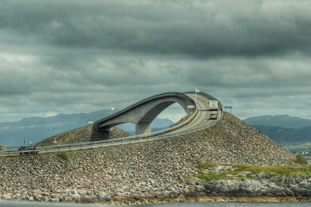 Two vehicles drive over a steep, dramatic bridge on the famous Atlantic Road in Norway near Alesund.