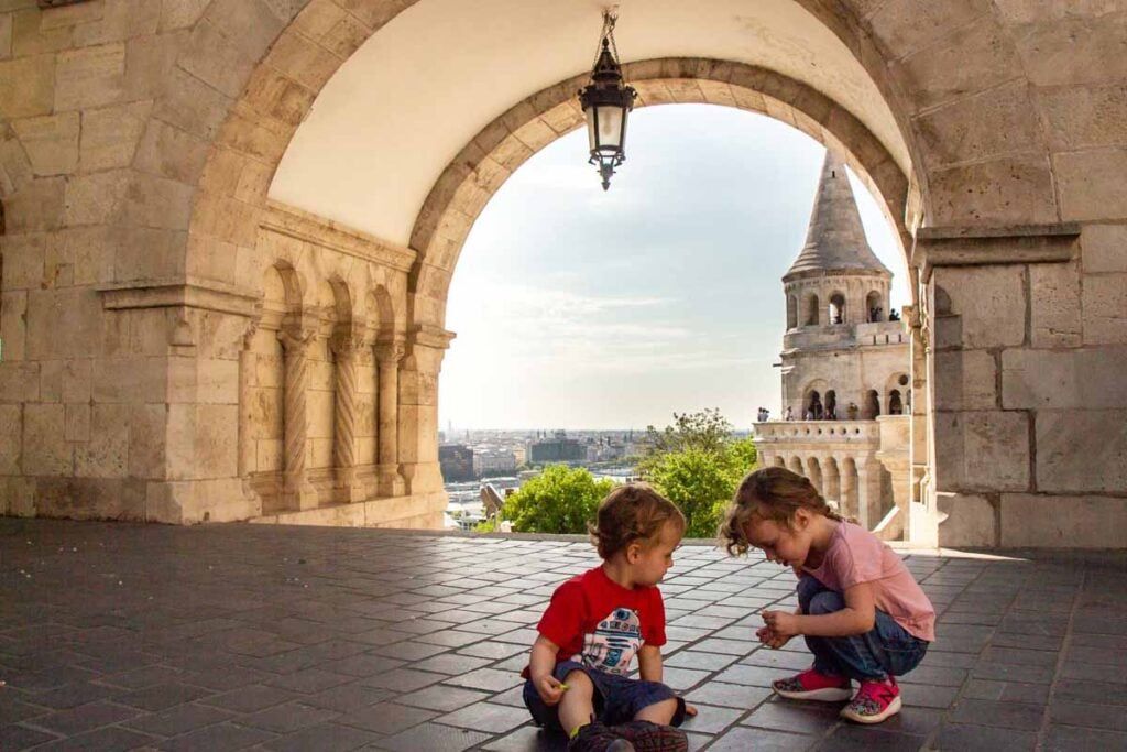 two small children on a family vacation to Budapest play on the floor in Fisherman's Bastion.