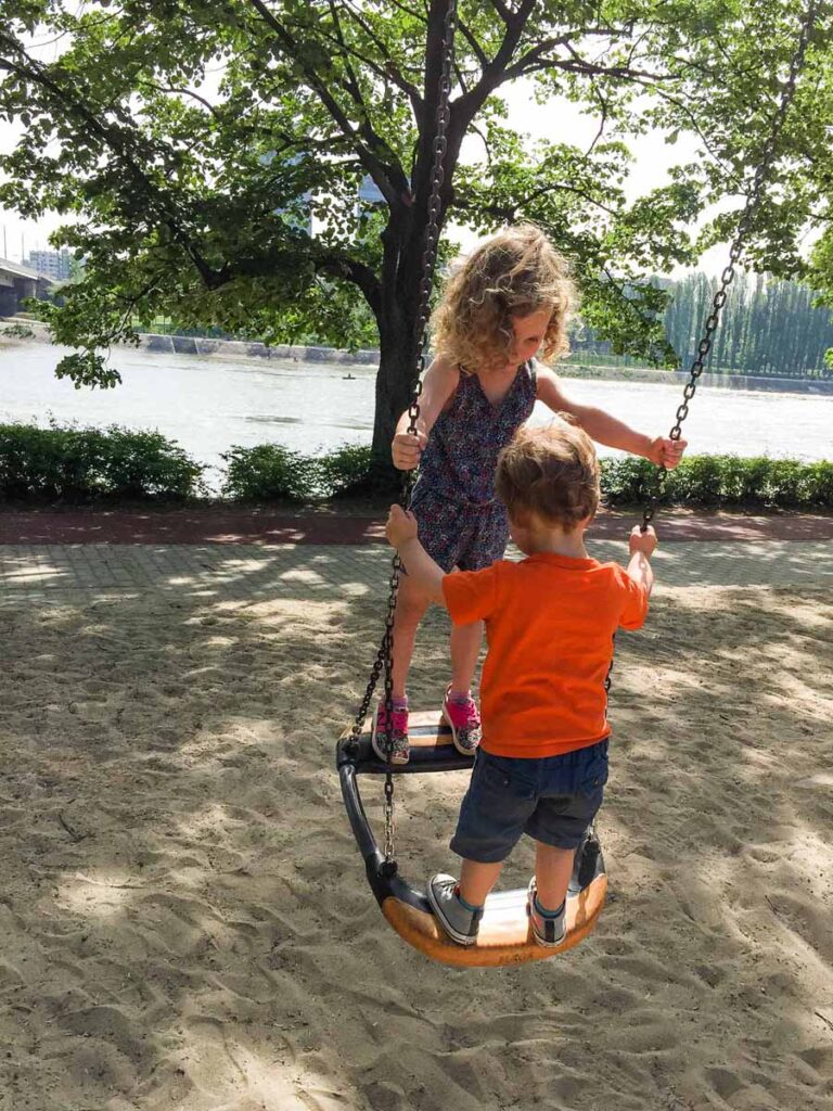 Two small kids play on a swing at a playground in Margaret Island, Budapest.