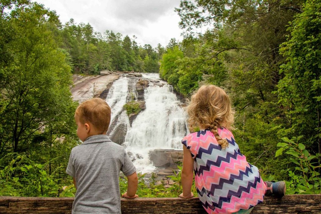 Two young hikers enjoy a waterfall on Triple Falls Hike in Dupont State PArk while on a family road trip in Asheville, North Carolina.