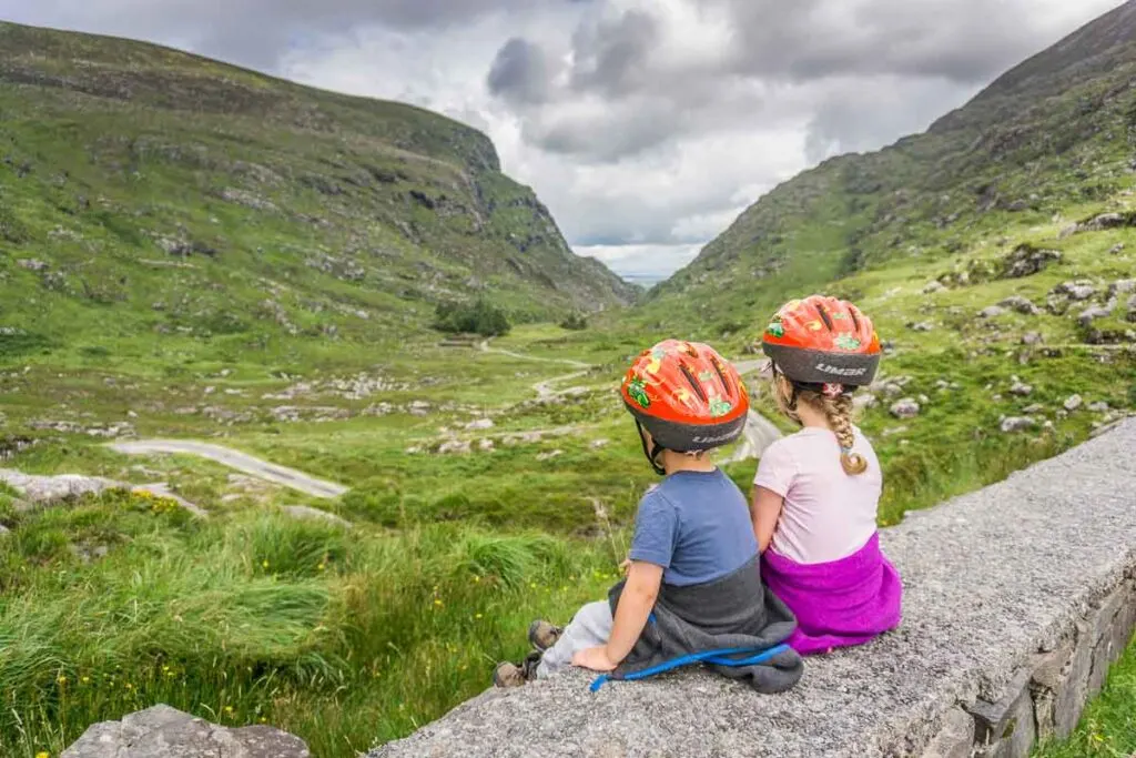 image of two children with helmets sitting on rock wall overlooking landscape below