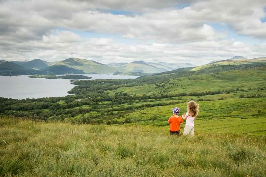 image of two kids standing in long grass looking at Loch Lomond in the distance