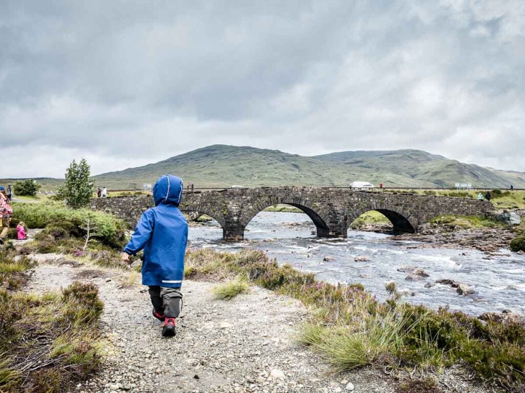 image of boy in blue rain jacket walking towards bridge on Isle of Skye