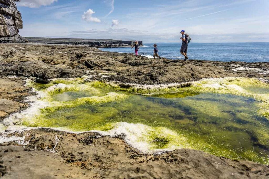 image of father and two kids walking along the ocean near the wormhole on Inishmore, which is one of the top things to see on Inis More Aran Island