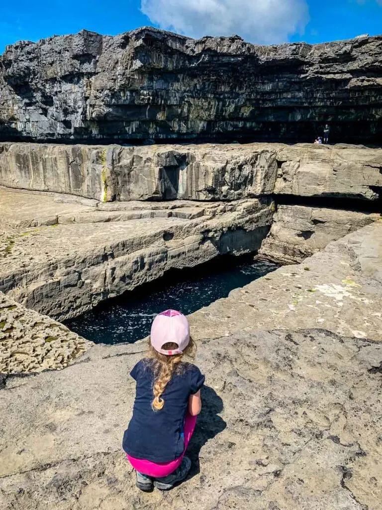 image of girl crouched down looking at the wormhole on Inishmore Island Ireland