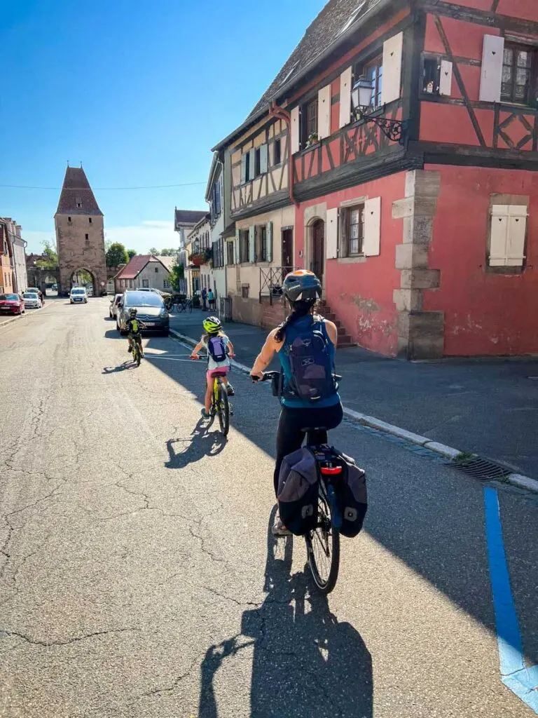 a family cycles through a colorful town with half-timbered houses in the Alsace wine region of France