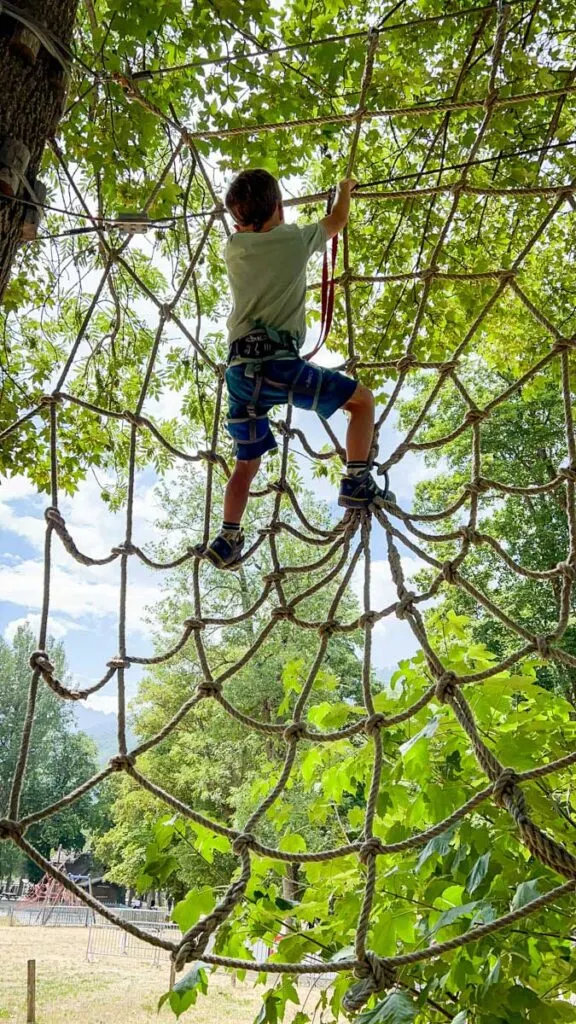 a 7 year old boy climbs a spider web made of rope at an adventure park in Briancon