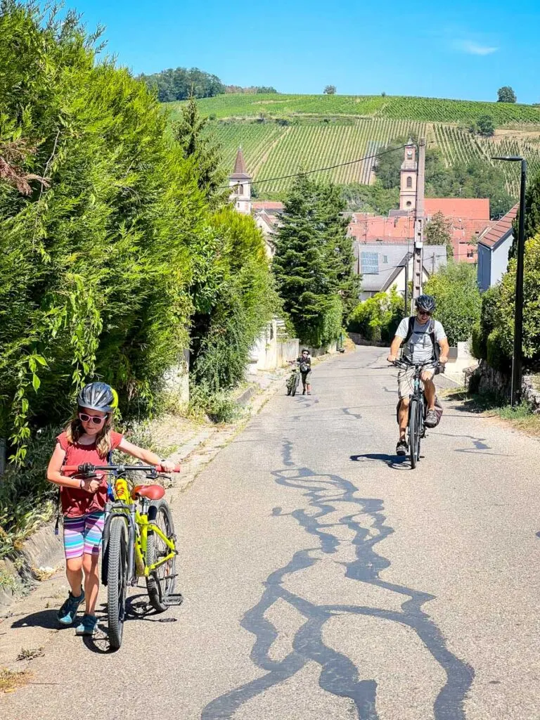 a girl pushes her bike up a steep hill while on a family cycling trip in France