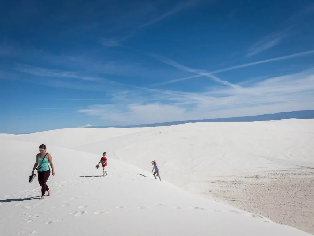 a family carries their shoes while walking barefoot on the Alkali Trail.