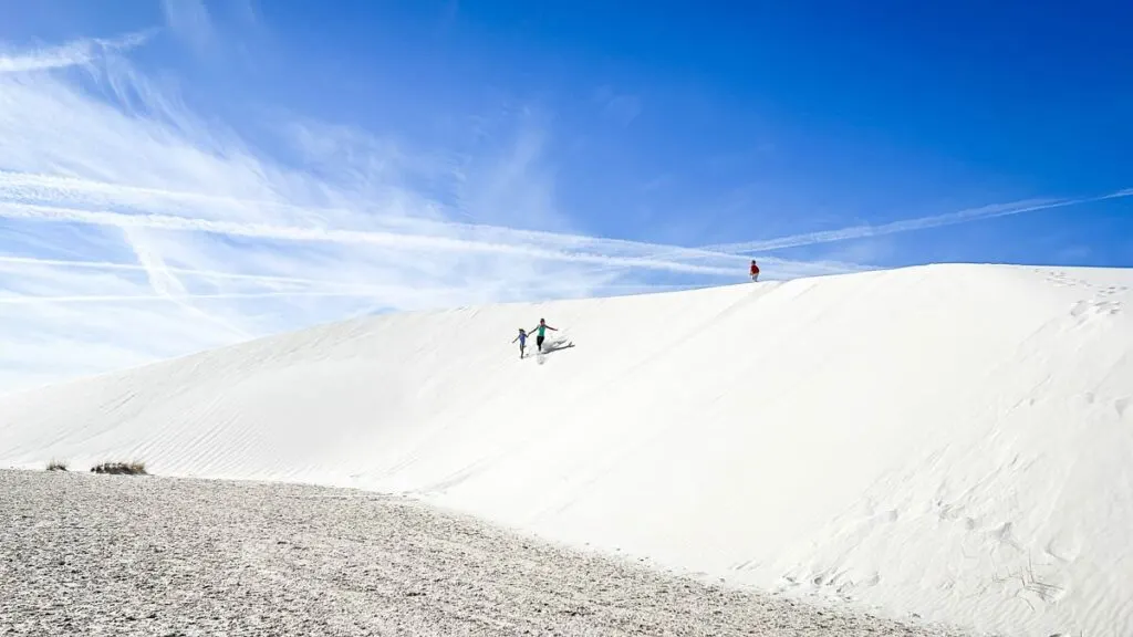 A family has fun running down a white sand dune in New Mexico.