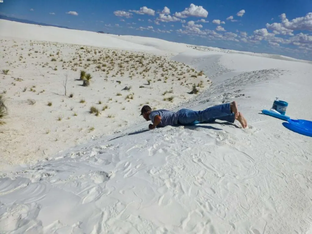 a man goes sledding on the sand dunes at White Sands, NM.
