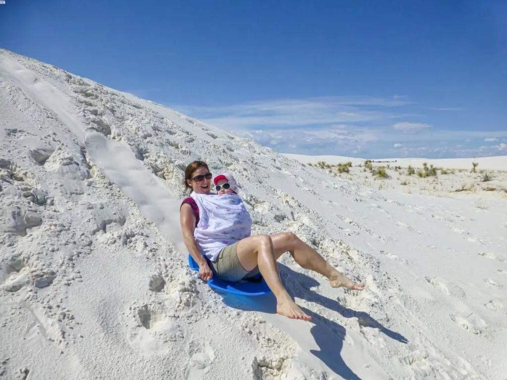 a mother holds her baby while trying to go dune sledding at White Sands National Monument (it wasn't a national park yet).