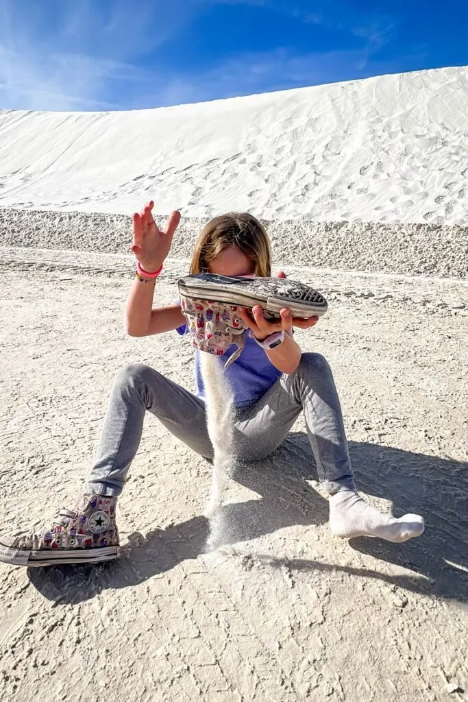 a girl empties all the sand out of her shoes after playing on the dunes at White Sands national park.
