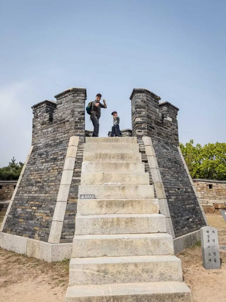 a father and son pretend to be archers on top of a defensive structure at the UNESCO Suwon Hwaseong Fortress.