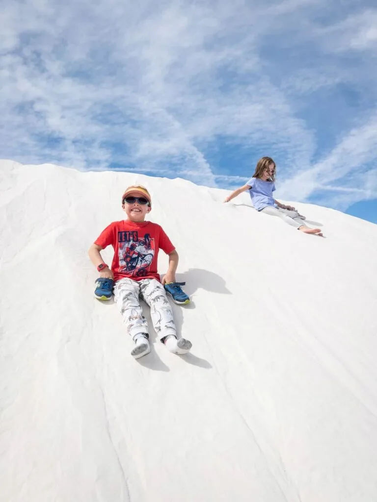 two kids slide down a white sand dune.