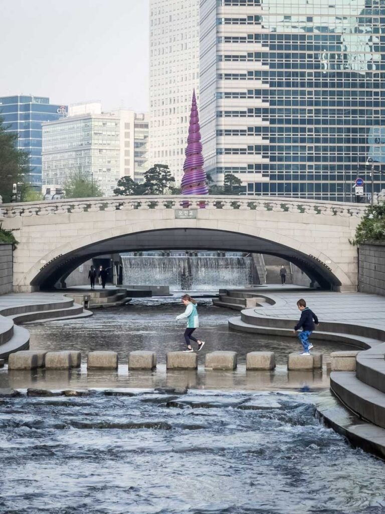 two kids have fun crossing the river over a stepping stone bridge in Cheonggyecheon River Park in Seoul, South Korea.