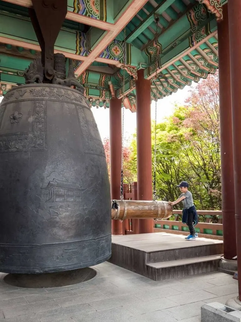 a young boy pulls back a large hammer to ring Hyowons Bell at the Suwon Fortress near Seoul.