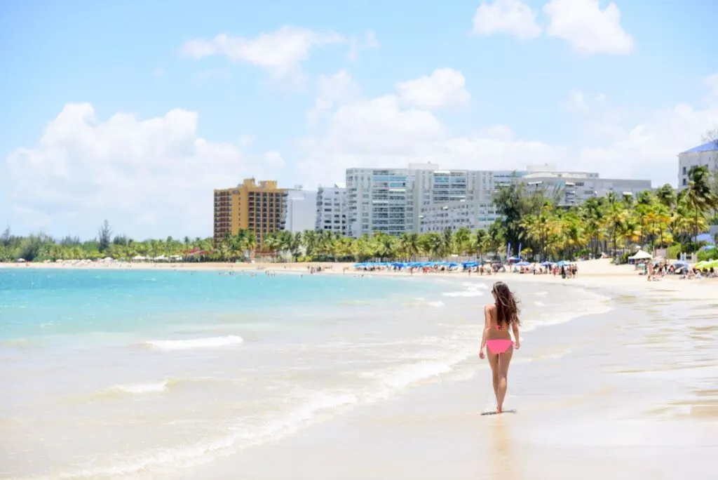 a woman in a pink bikini walks on the sand at the kid-friendly Isla Verde Beach in San Juan, Puerto Rico.
