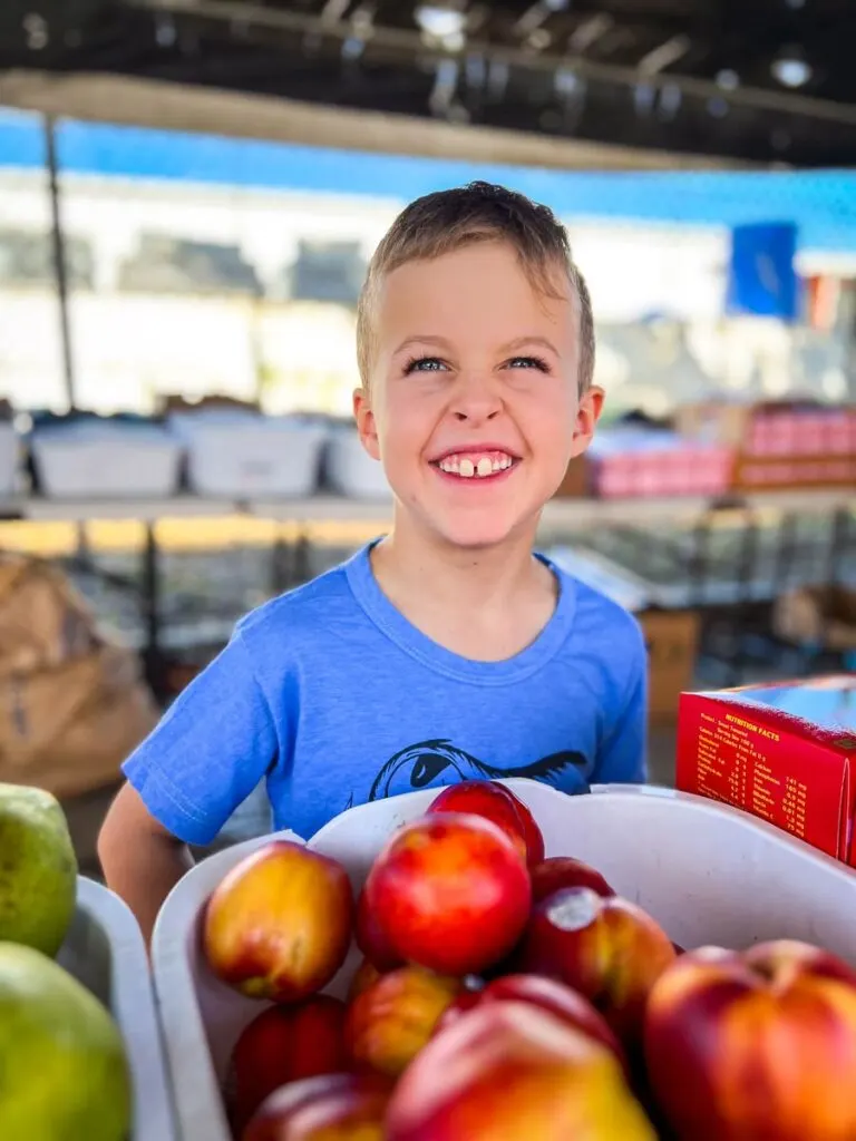 a very happy boy in front of a bin of nectarines at a fruit market in Vieques.