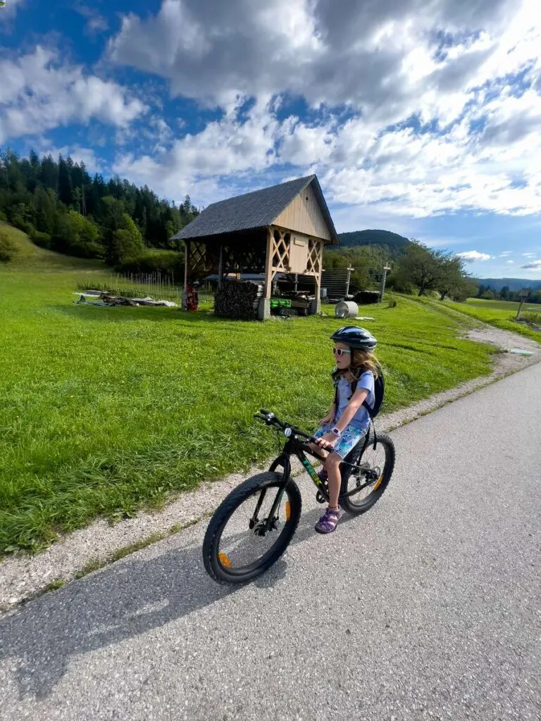 a young girl rides her bike past an elevated hut in the Slovenian Alps.