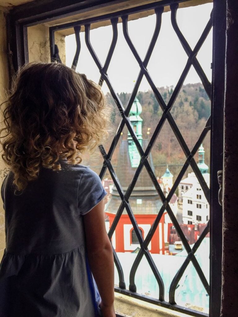 a 4-year old girl looks down at the town from the tower in the Loket Castle.