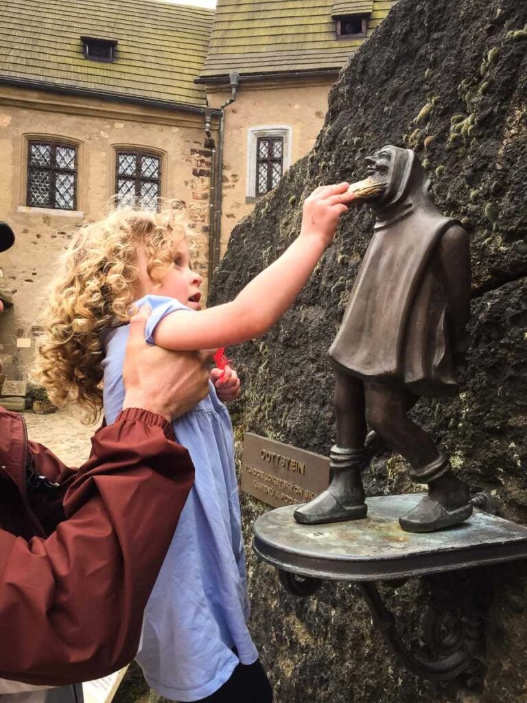 a 4-year old girl rubs the beard on a bronze statue in Loket, Czech Republic.