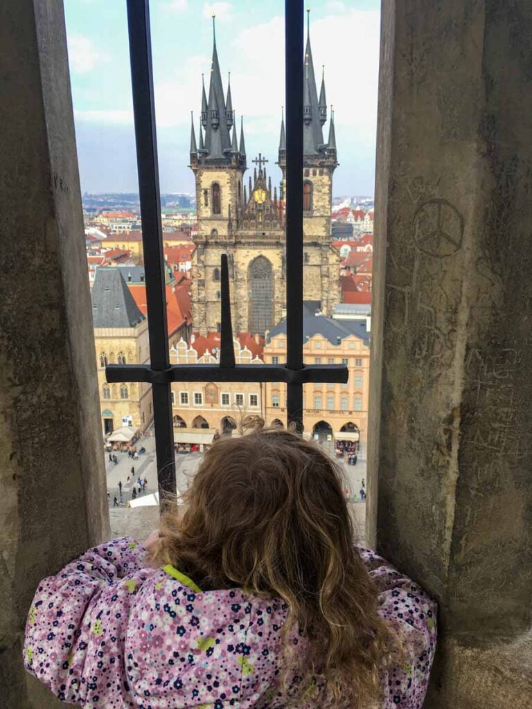 a young girl looks out at the city of Prague from a window in the Old Town Hall in Prague.