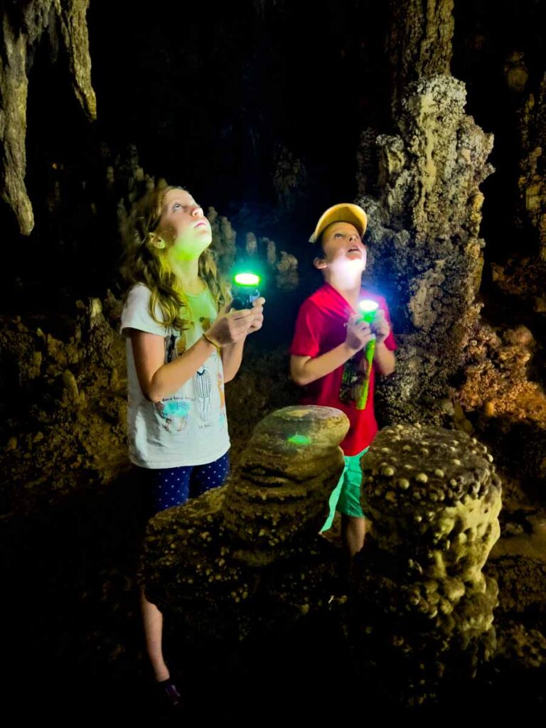 two kids hold flashlights while on a tour of The Pa Ka Rang Cave (Coral Cave) in Khao Sok National Park.