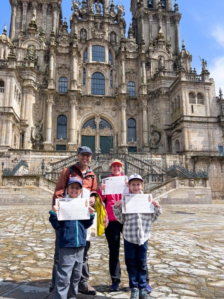 The FamilyCanTravel.com family show off their certificates for completing the Portuguese Coastal Camino pilgrimage while standing in front of the Cathedral de Compostela.