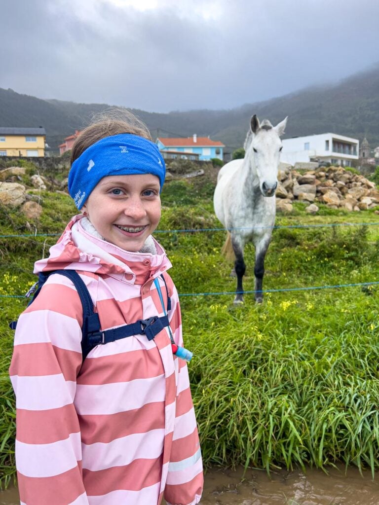 A 10-year old girl is excited to meet a beautiful white horse along the Portuguese Coastal Camino Trail in Oia, Spain.