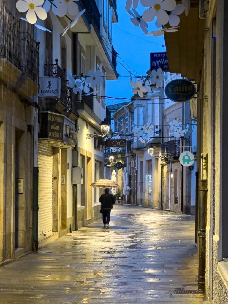 A person with an umbrella walks through the deserted streets of Padron, Spain in the early morning on a rainy day.