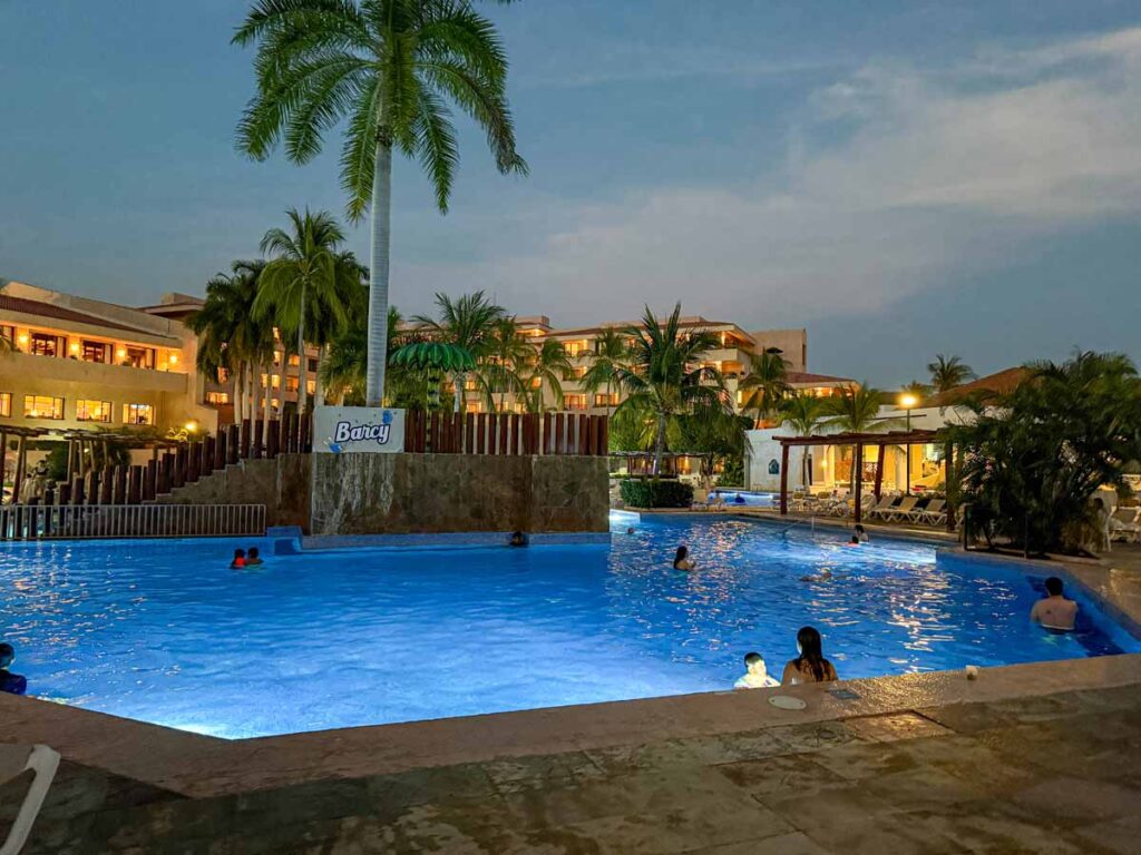 a swimming pool at the Barcelo Huatulco all-inclusive resort is softly lit at night.