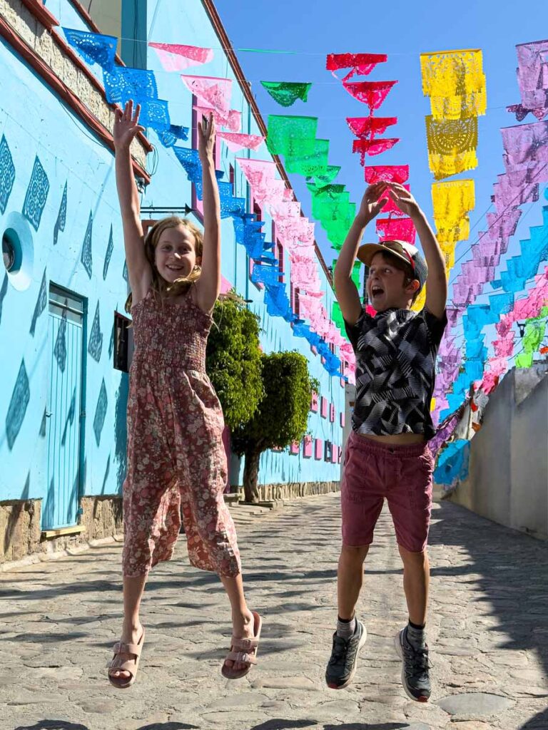 The kids from FamilyCanTravel.vom, jump in the air in the vibrant Jalatlaco neighborhood in Oaxaca, Mexico.