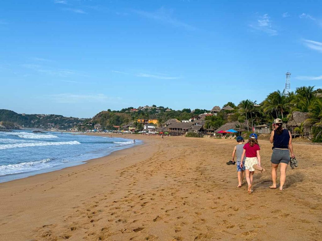 Celine Brewer, owner of FamilyCanTravel.com, walks on the golden sand of Playa San Agustinillo with her kids during a family trip to Oaxaca, Mexico.