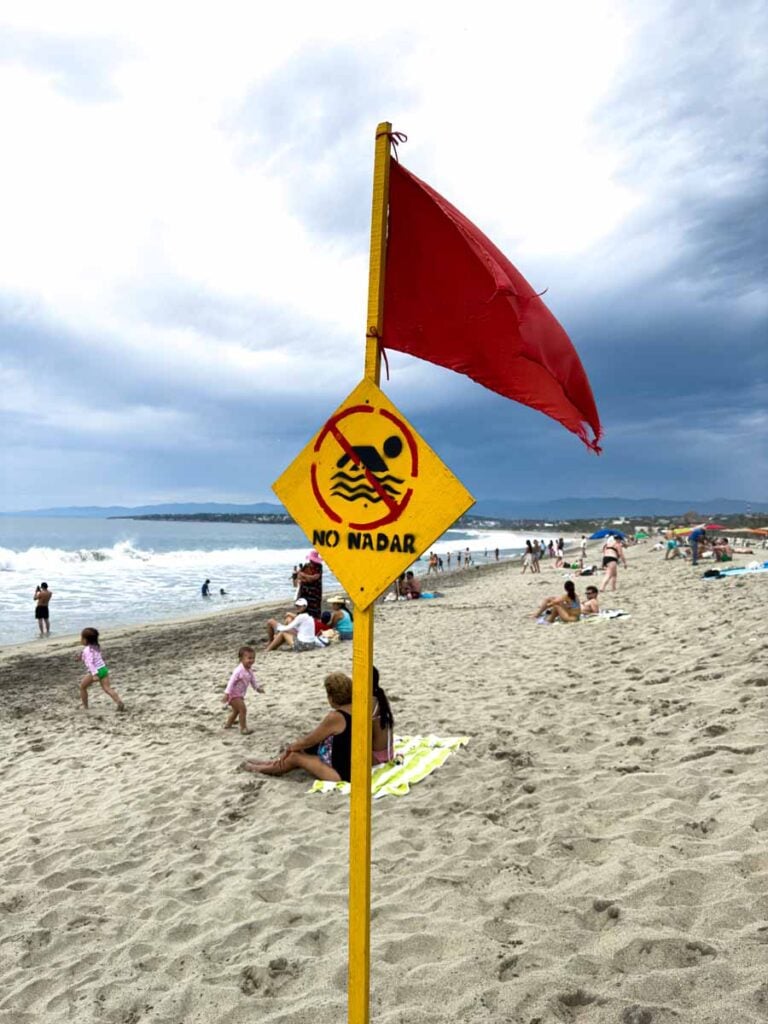 a red flag and a no swimming sign on the beach at Playa Zicatela in Puerto Escondido, Mexico.