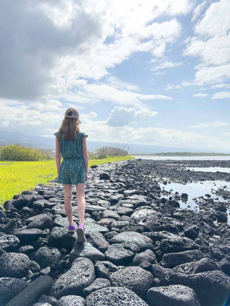 an 11-year old girl on a family vacation to Hawaii walks on midnight black rocks on the hiking trail around Kaloko-Honokohau National Historic Park.