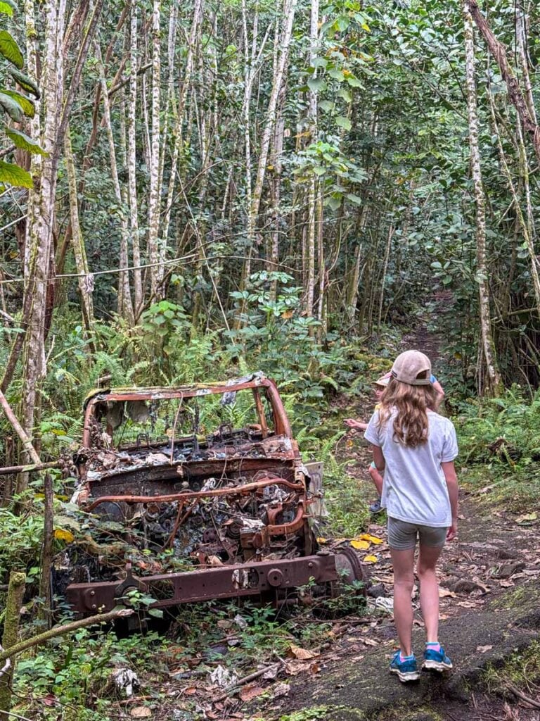 An 11-year old girl hikes past an abandoned car which is being reclaimed by the forest on the Puna Trail on the Big Island of Hawaii.