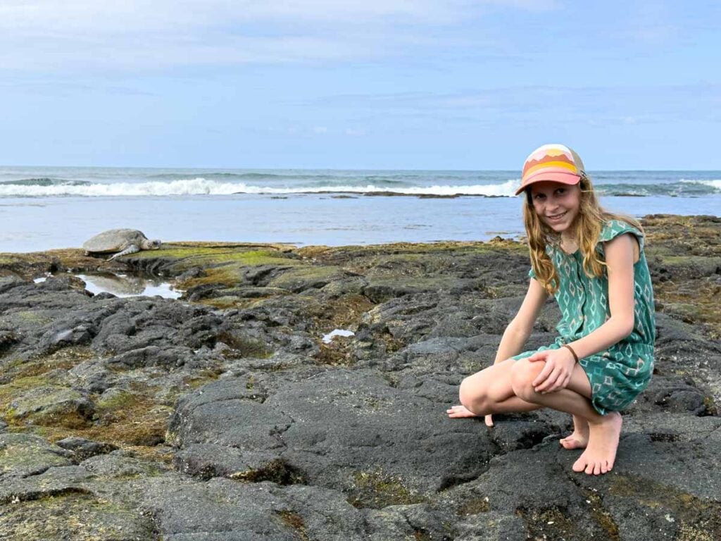 An 11-year old girl on a family hike at Family Friendly Hikes on Hawaii - Kaloko-Honokohau National Historic Park admires a sea turtle on the rocks.