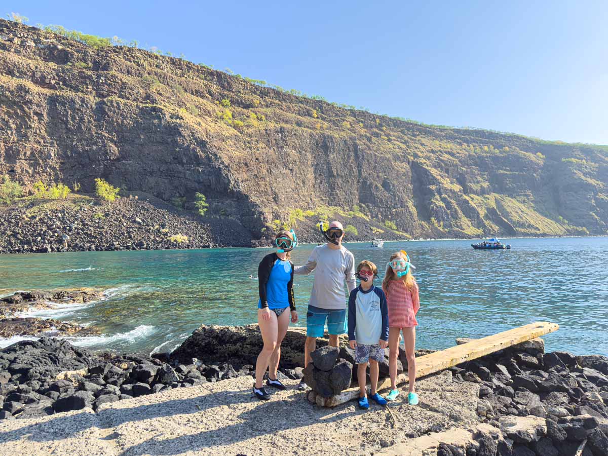 The Brewer family, from the Family Can Travel blog, stand with their snorkel gear on at the Captain Cook Memorial, the best place to go snorkeling with kids on the Big Island.