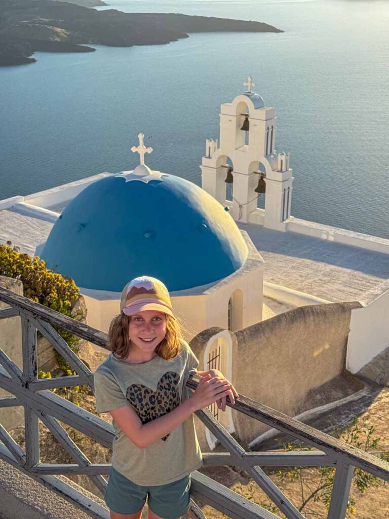 an 11-year old girl enjoys watching the sun set over the caldera at the Three Bells of Fira on Santorini, Greece.
