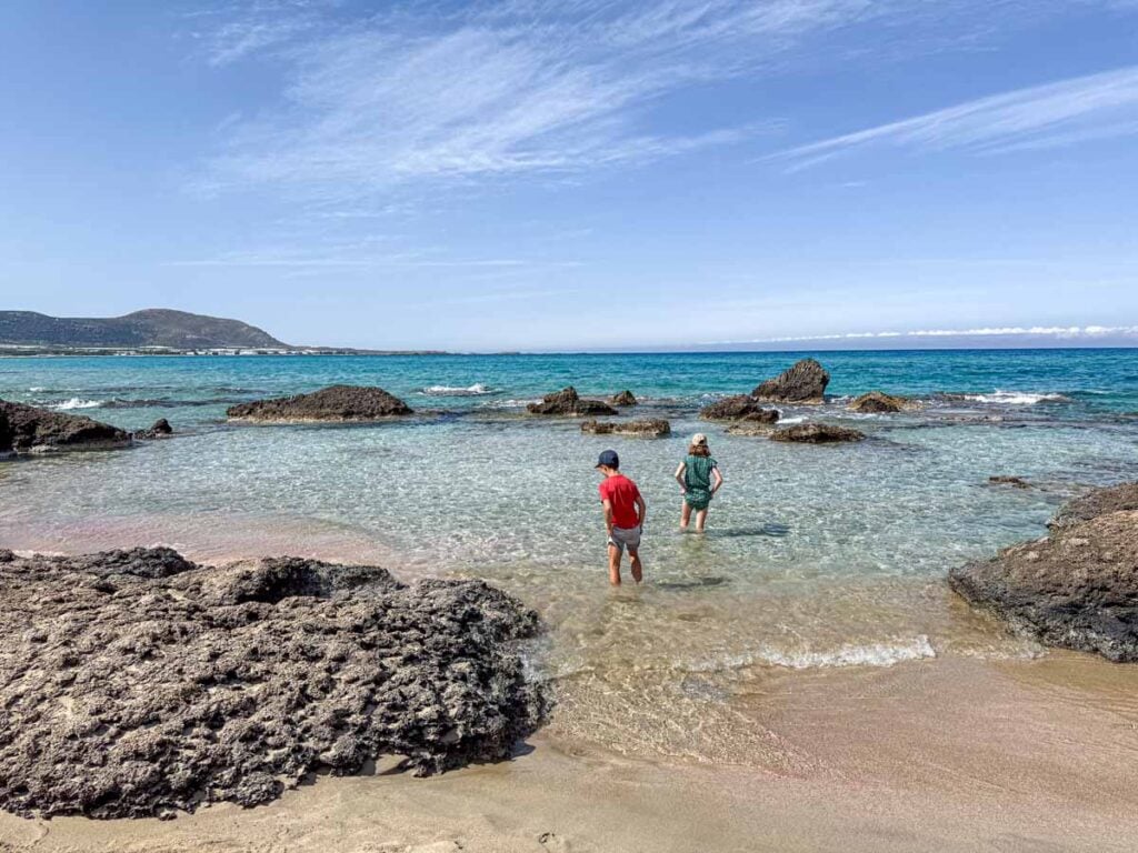 two kids play in a small cove at Falassarna Beach - one of the best beaches for families on Crete.