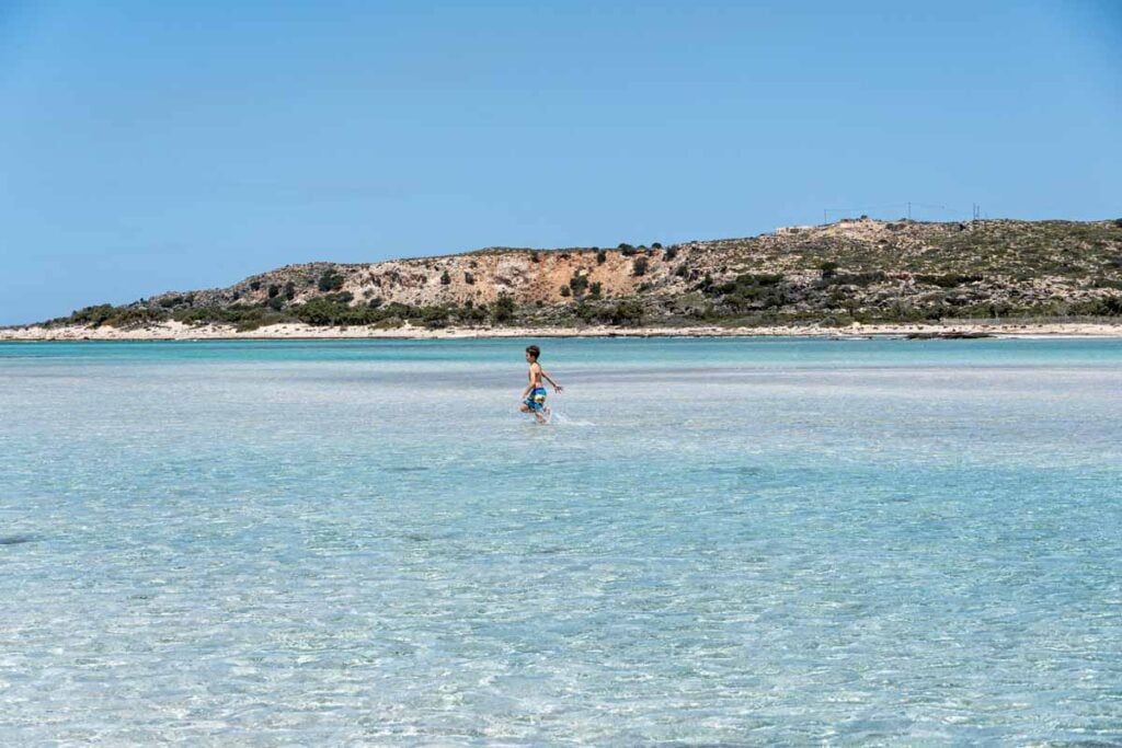 A 9-year old boy walks through turquoise water at Elafonisi Beach - the best family-friendly beach on Crete.