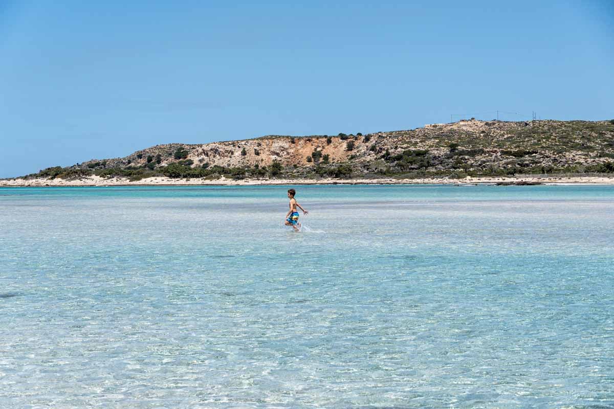A 9-year old boy walks through turquoise water at Elafonisi Beach - the best family-friendly beach on Crete.
