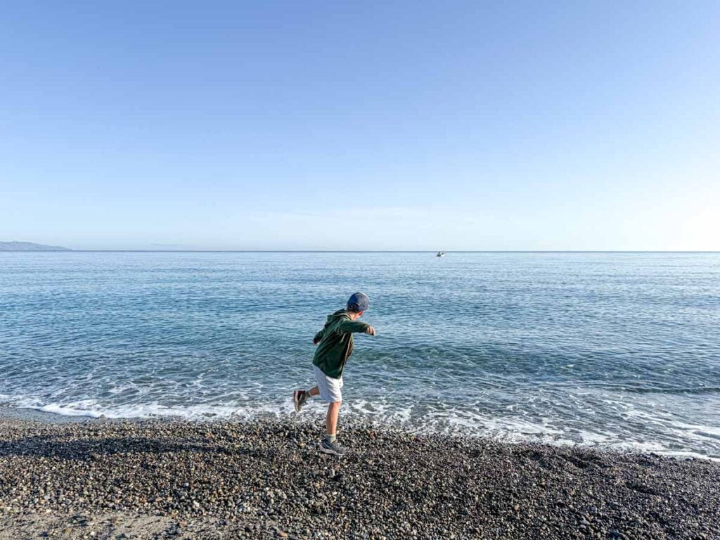 a 9-year old boy throws rocks into the ocean on Kostakis Beach while on family vacation to Crete, Greece.